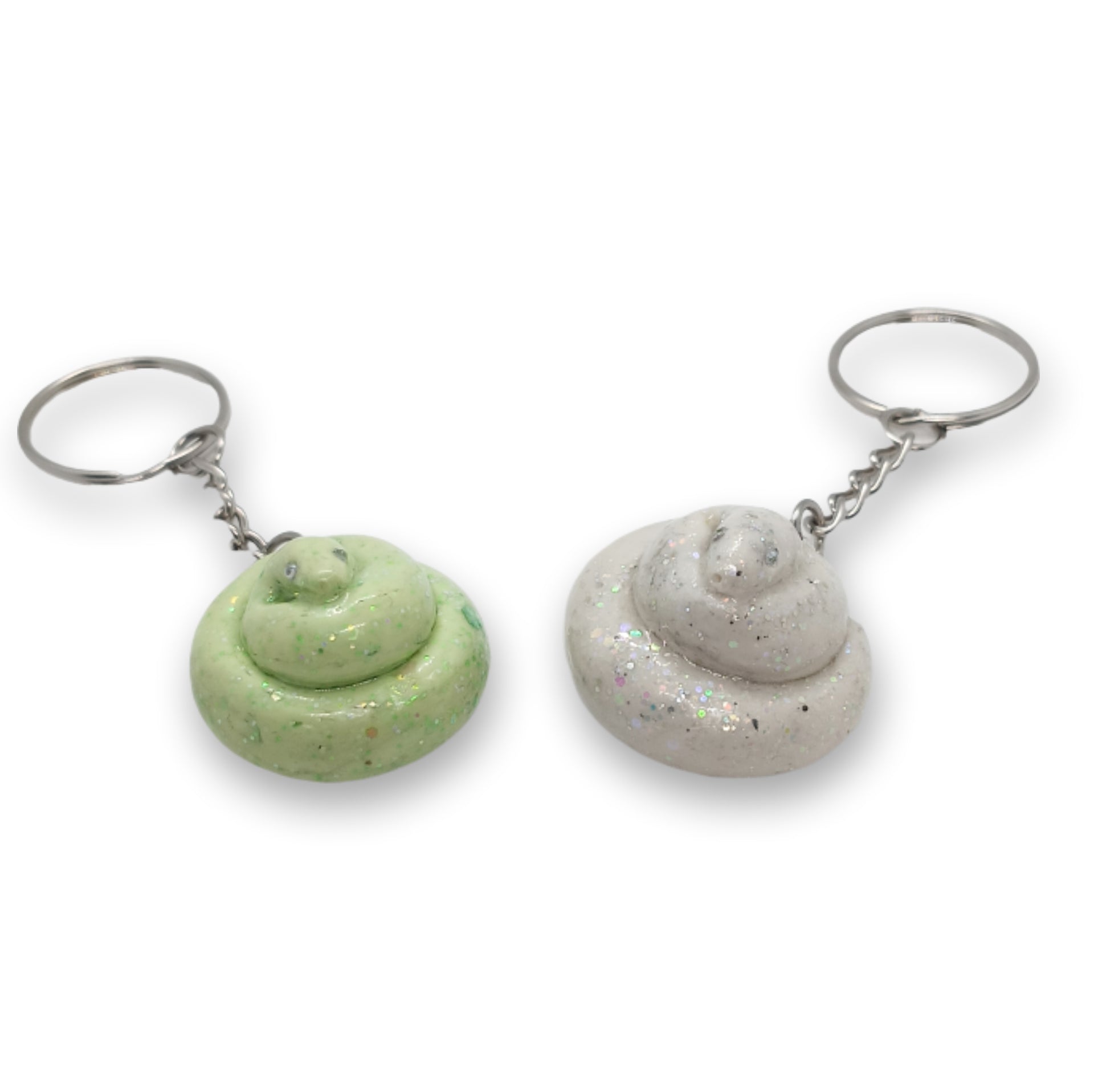 Two novelty poop-shaped keychains on a plain white background. One keychain is light green with darker green speckles, and the other is light gray with fine silver glitter.