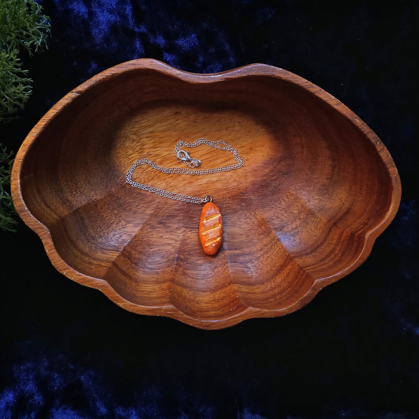 Wooden bowl with a silver necklace and baguette pendant on a dark background