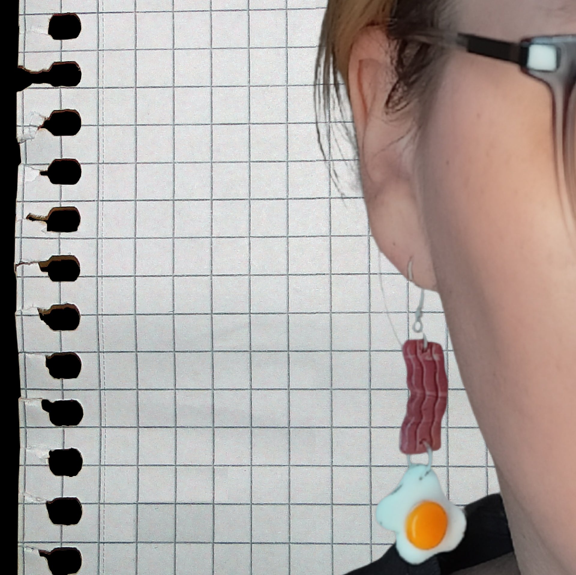Person wearing earrings shaped like bacon and an egg against a grid background