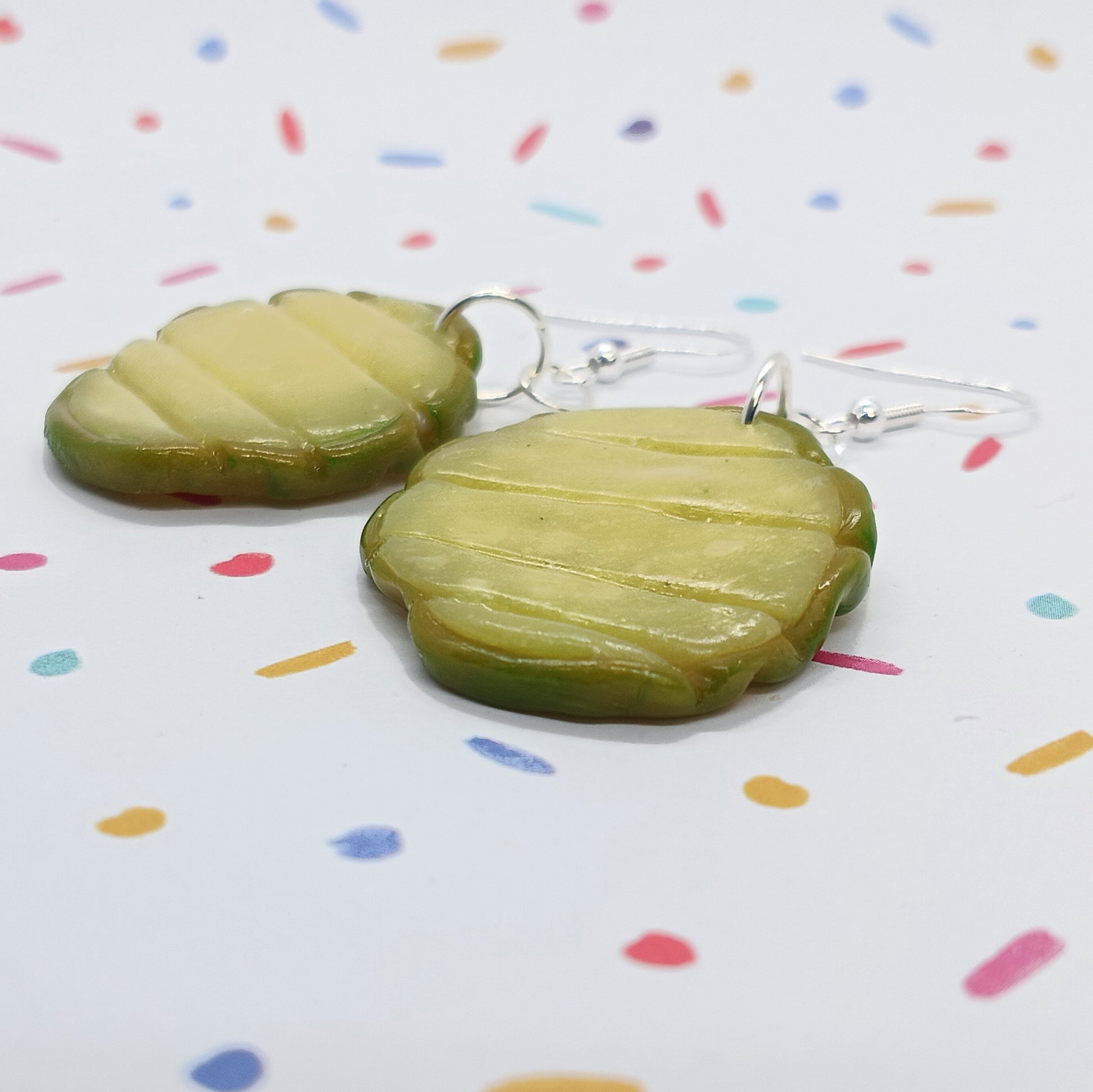 Pickle-shaped drop earrings with silver fishhook wires, displayed on a white background with colorful confetti dots.
