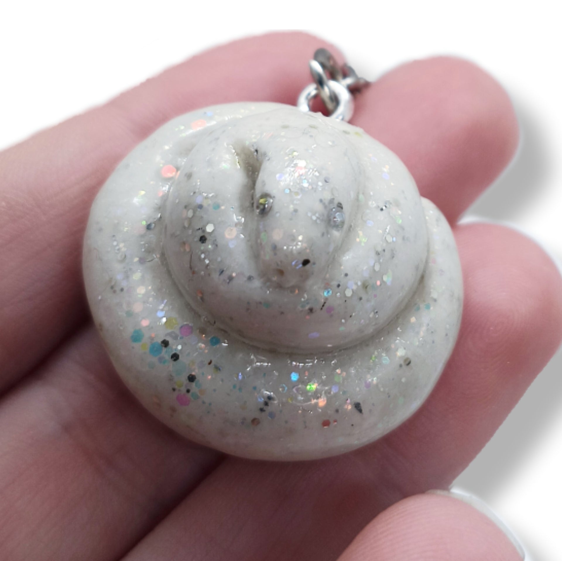 A small coiled poop-shaped charm or pendant with embedded glitter, held in a person's hand against a white background.