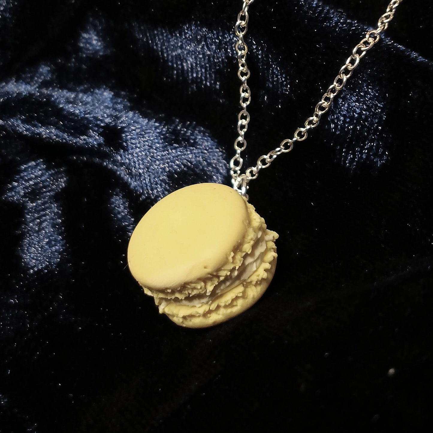 Yellow macaron-shaped pendant on a chain against a dark blue velvet background